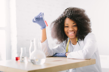 Young beautiful African American girl doctor in a white coat with a stethoscope. sitting at a table...
