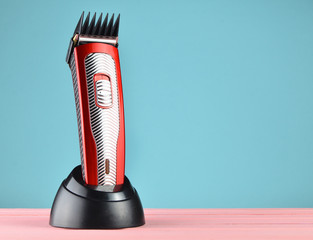 Wireless clipper with a nozzle stands on a charging station on a pastel background, copy space.