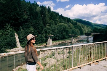 Fototapeta na wymiar Beautiful brunette girl in hat is walking with green mountains on background