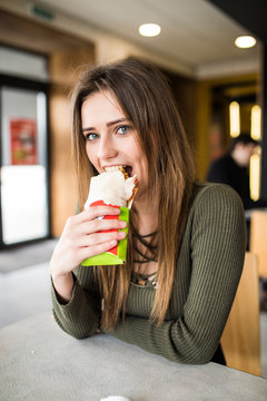Young hungry woman sitting in a restaurant eating an doner hand hold- hunger, food, meal concept