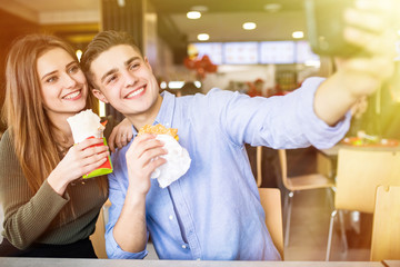 Happy smiling woman and a handsome man are enjoying their delicious and tasty burgers and doner taking selfie phone