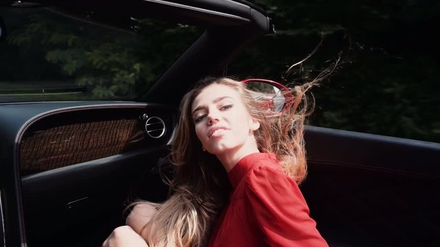 Beautiful sexy fashion girl model with bright makeup in luxury car. Beautiful woman enjoying ride in convertible vintage car on road trip with outstretched arms.