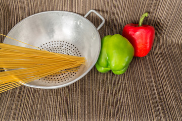 Silver strainer with raw spaghetti and red and green peppers