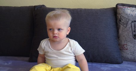 Toddler boy sitting on the couch, blond, blue eyes, watching TV.