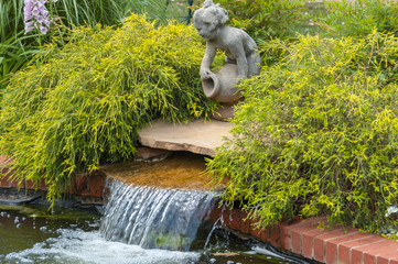 Stone statue of a laughing child with a jug above a water feature among green shrubbery