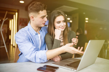 Happy young couple is using a laptop, drinking coffee and smiling while sitting at the cafe