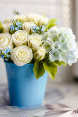 Exquisite spring bouquet. Blue and white wedding flowers. Wedding floral decorations. Floristic composition in a sky-blue vase. Roses, lilies and violets. Macro close up. Perfect girl gift idea