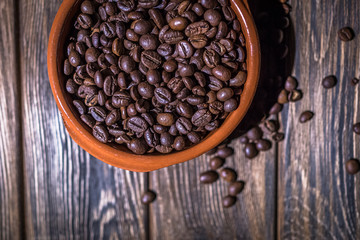 The roasted coffee beans lie in a large ceramic plate on a wooden table