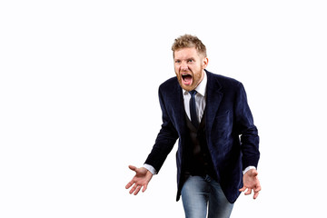 a young guy with a beard and a dark blue suit and light jeans is very angry and screams raising both hands up