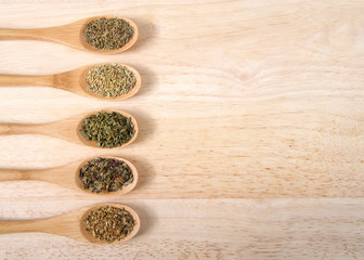 Wooden spoons with traditional Italian herbs for cooking on a light wood table.