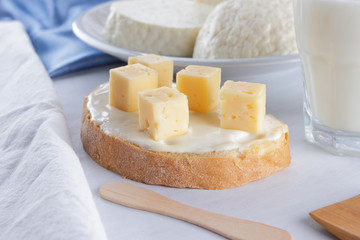 Cheese, dairy assortment on a white background, sandwich with soft cheese on a blue napkin, wooden background, wooden cutlery, top view, white cheese on a white plate, kefir in a glass, pop art