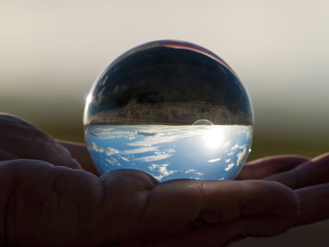 Woman hand holding glass ball with panoramic view of countryside and sky/ Concept for environment