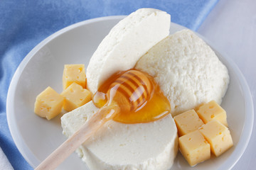 Cheese, milk assortment on white background, white cheese and honey on a blue napkin, wooden background, wooden stick for honey, top view, cheese on white plate, kefir in a glass, pop art