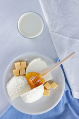 Cheese, milk assortment on white background, white cheese and honey on a blue napkin, wooden background, wooden stick for honey, top view, cheese on white plate, kefir in a glass, pop art
