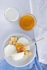 Cheese, milk assortment on white background, white cheese and honey on a blue napkin, wooden background, wooden stick for honey, top view, cheese on white plate, kefir in a glass, pop art