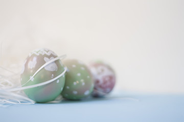 Easter background in pastel colors: handmade hand painted festive eggs pink and green, decorative polka dots doodles, white straw, blue backdrop. Bright colorful composition, blurred, selective focus.
