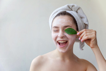 Beauty portrait of a smiling brunette woman in a towel on the head with white nourishing mask or...