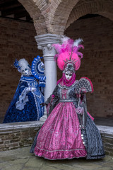 Fototapeta na wymiar Masked women in ornate blue and pink costumes with fans in an inner courtyard during the Venice Carnival (Carnivale di Venezia)