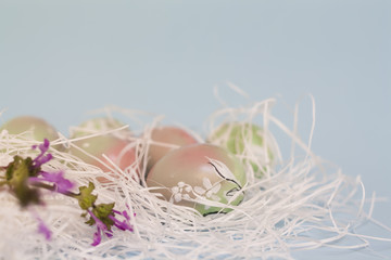 Easter background in pastel colors: handmade hand painted eggs in pink and green gradient, decorative bunny doodles, white straw, blue backdrop. Bright colorful composition, blurred, selective focus.