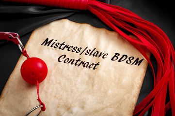 BDSM contract or “slave contract” concept with sex toys, ball gag and a flogger around an old...