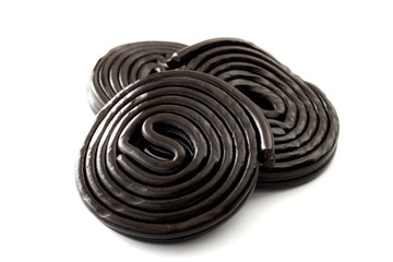 Black liquorice spirals, chewy candy and delicious dessert concept with licorice wheels which are flavoured with the extract of the root of the Glycyrrhiza glabra plant, isolated on white background