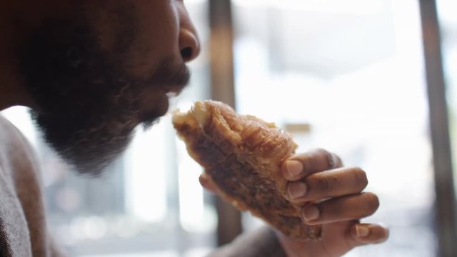 Mature black man in a suit takes a bite from his almond croissant