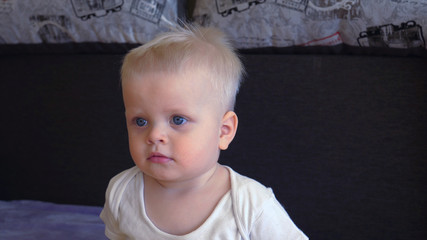 Toddler boy sitting on the couch, blond, blue eyes, watching TV.