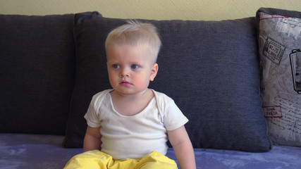 Toddler boy sitting on the couch, blond, blue eyes, watching TV.