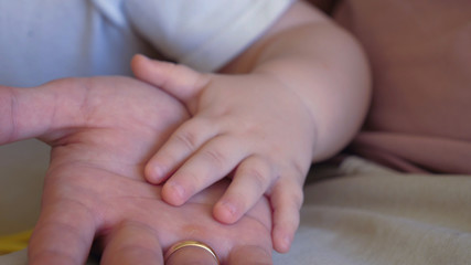 Father and baby boy holding hands at home.