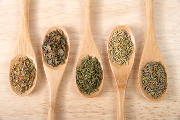 Wooden spoons with traditional Italian herbs for cooking on a light wood table. Can be horizontal or vertical
