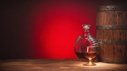 Glass of cognac with barrel on red backgroun