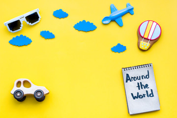 Travelling with child concept. Air balloon, car and plane. Around the world hand lettering in notebook on yellow background top view copy space