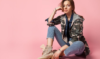 Portrait young woman  on a pink background in jeans, military jacket and in rough shoes. Fashion model in casual clothes.