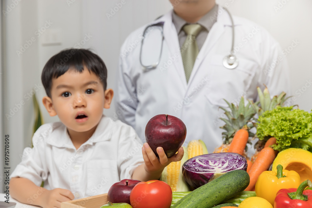 Wall mural Healthy and nutrition concept. Kid learning about nutrition with doctor to choose eating fresh fruits and vegetables. Young asian boy holding apple.