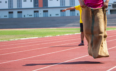 Friends having fun,young men playing sack race in city park 