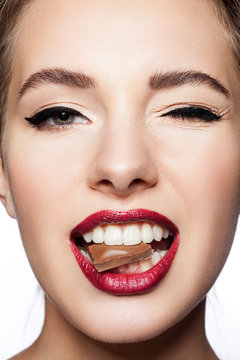 Close-up face model with red lips and black arrows on eyes. Beautiful woman with a slice of chocolate in her mouth