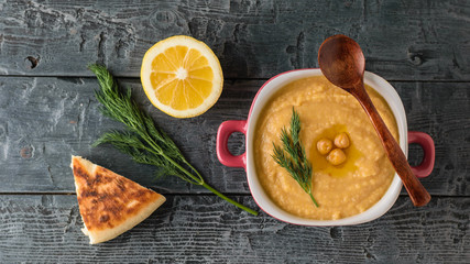 Freshly made hummus in a purple bowl on a table with a piece of bread. The view from the top.