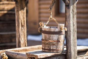 old wooden bucket of water hanging over the well with a wooden building