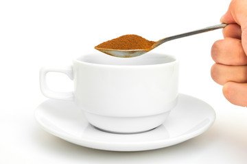 hand holding teaspoon and instant coffee for pouring into ceramic cup on white background