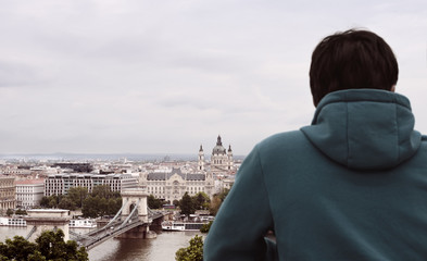 Back view of young man on mountain top looking at city with daylight