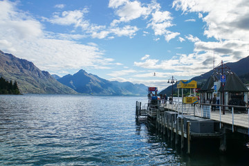 Queenstown / New Zealand - November 2 2017: Editorial wooden walkway to pier for passenger boat with mountain range in blue sky backdrop