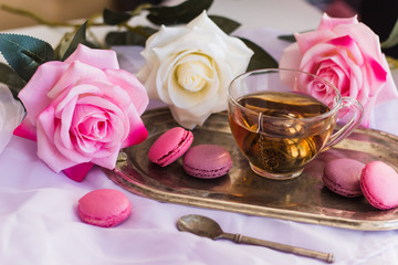 pink macaroons, hot tea on silver vintage tray blurred roses background