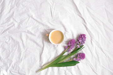 Obraz na płótnie Canvas Cup of coffee and lilac hyacinth flowers on cotton sheet. Flat lay, top view