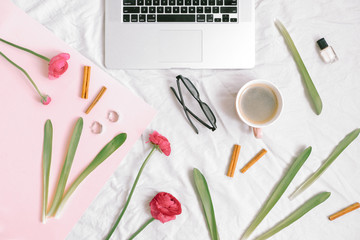 Laptop, flowers, cup of coffee and feminine accessories on cotton sheet. Home office concept. Flat lay, top view