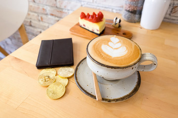 Golden bitcoin being main Cryptocurrency digital payment system with hot latte coffee, wallet and cake on wooden table background. A concept for electronic currency can be used in the shop.
