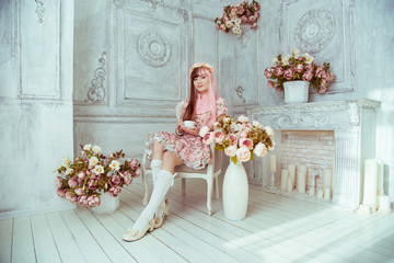 Beautiful young woman doll in a pink dress, in a bright room and flowers sitting in a chair with a cup, tea party, lolita. Japanese street fashion.