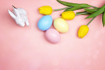 Fototapeta na wymiar Easter holiday background concept. Colorful eggs, bunny and yellow tulips on pink paper. Space for text.