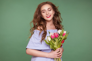 Beautiful young girl with a tulip bouquet standing on a green background. Women's Day, March 8th.