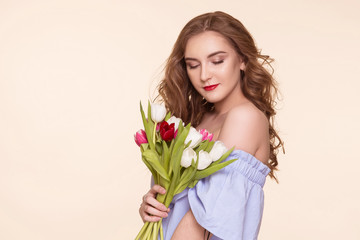 Beautiful young girl with a tulip bouquet standing on a beige, background, in a blue dress. Women's Day, March 8th. Copy-space.