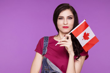 Beautiful brunette woman holding a flag of canada in her hands, on a purple background. Learning a...